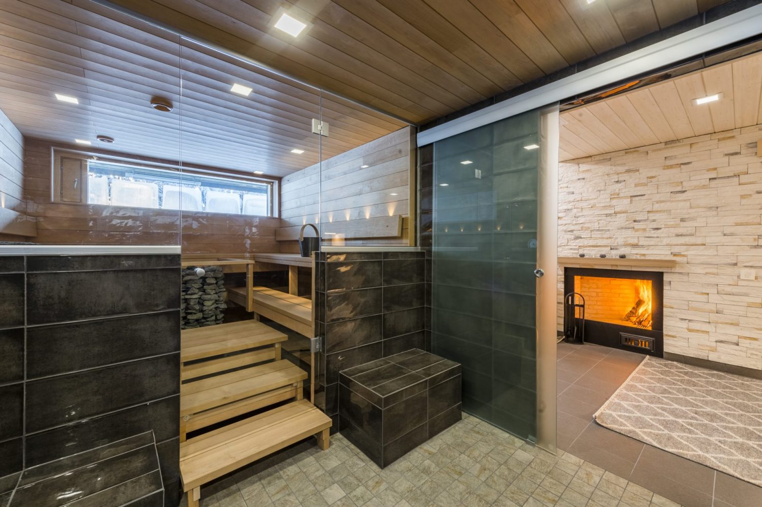 Sauna lasiseinän takana, lauteet ja viereinen takka
